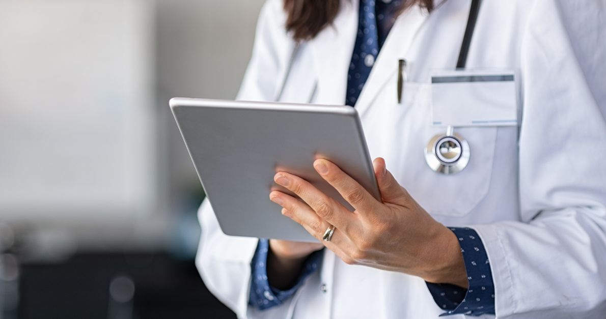 Close-up of a healthcare professional in a white coat using a tablet, stethoscope visible—illustrating digital clinical study report automation.