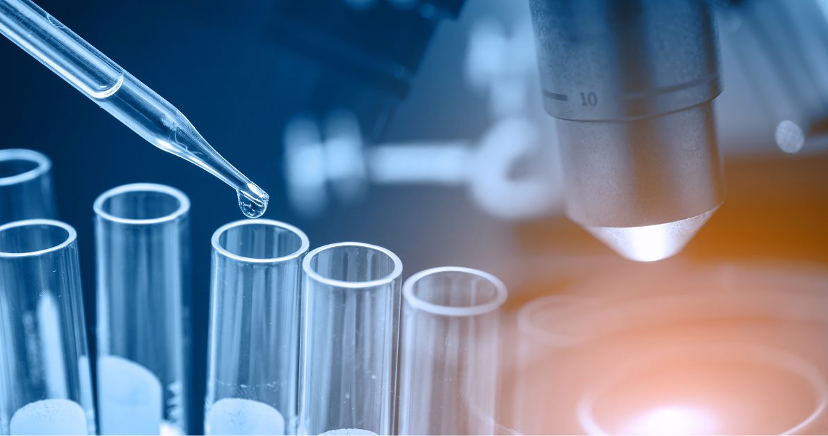 Close-up of a laboratory pipette dispensing liquid into glass test tubes beside a microscope, with a blue and orange background.